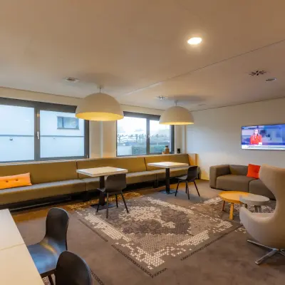 Modern office space for rent at Marshalllaan 2, Delft, featuring cozy seating, tables, and a television, ideal for office space rental activities.