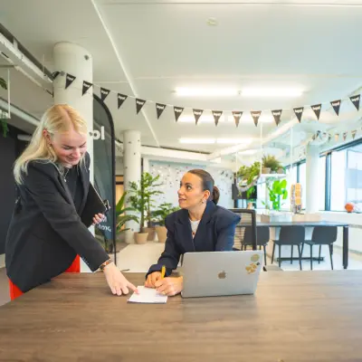 Two people in a modern office at Hambakenwetering 1, Den Bosch are engaged in a business discussion in a lively workspace, ideal for office space rental.
