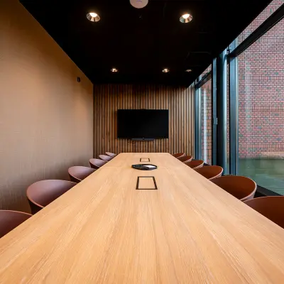Modern conference room at Hambakenwetering 5 with a long wooden table, surrounded by chairs and a wall-mounted screen, ideal for office space rental in Den Bosch.