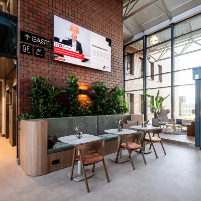 Modern office space at Hambakenwetering 5 in Den Bosch with stylish furnishings, indoor plants, and a wall-mounted screen. Perfect for office space rental, it features natural lighting and a comfortable seating area.