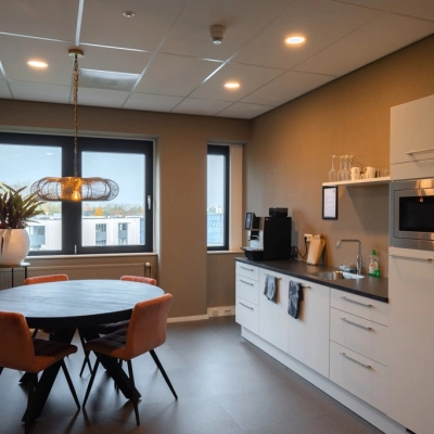 Modern office kitchen area at Keulenstraat 1, Deventer, available for office space rental, featuring a round table with chairs, microwave, and coffee machine.