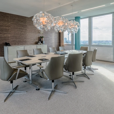 Spacious conference room for office space rental at Dreischeibenhaus, Düsseldorf. It features modern chairs, a large table, and decorative lighting with a city view.