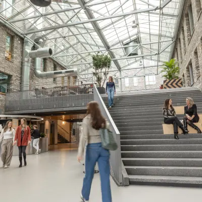 Modern office atrium at Flight Forum 120-159, Eindhoven Airport, featuring a glass ceiling, spacious staircase, and people engaged in business activities. Ideal for those seeking office space rental with a contemporary vibe.