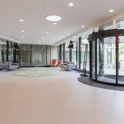 Spacious office entrance at Professor Dr Dorgelolaan 14, Eindhoven Center, featuring modern seating and a revolving door. Ideal office space rental for a professional yet inviting atmosphere.