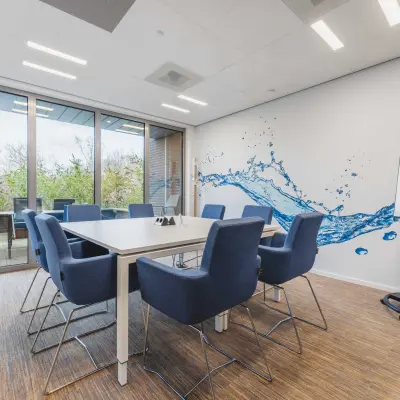 A modern conference room with a large table, blue chairs, and a glass wall in an office space available for rent at Hurksestraat 60, Eindhoven De Hurk.