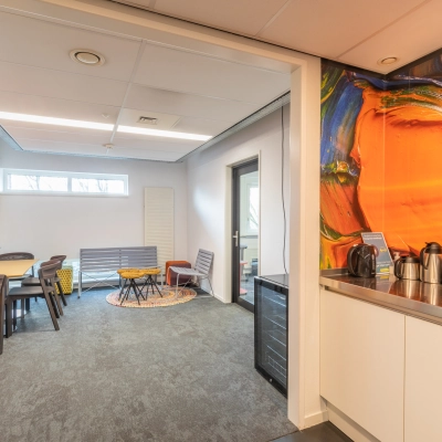 Vibrant office lounge at TU campus, De Zaale 11, Eindhoven. Features colorful mural walls, seating area with chairs and tables, and kitchenette. Ideal for office space rental enthusiasts seeking a dynamic environment.