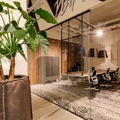 Modern office space available for rent at Frederiklaan 10E, Eindhoven Strijp-S, featuring a stylish meeting area with glass walls, wooden accents, and a large plant for ambience.