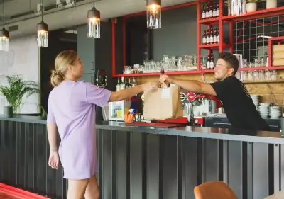Two people interact at a modern bar area within an office at Torenallee 20, Eindhoven Strijp-S, showcasing opportunities for office space rental.