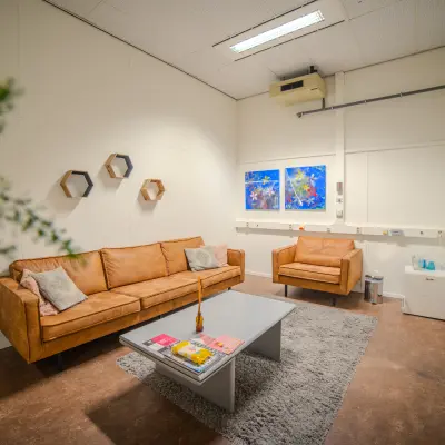 Furnished office lounge at Torenallee 20, Eindhoven Strijp-S, featuring comfortable seating, a coffee table, and wall art. Ideal office space rental.