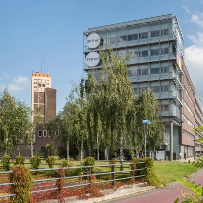 Exterior view of the office building at Brandweerstraat 20-30, Enschede, showcasing modern architecture with large windows. Ideal for office space rental, surrounded by greenery and a bike path in front.