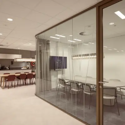 Modern office space available for rent in Enschede, featuring a conference room with glass walls and a furnished common area including tables and chairs.