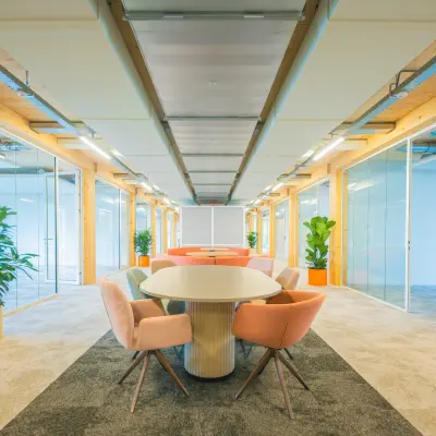 Bright and inviting office space rental in Enschede featuring a long table with chairs, surrounded by glass-partitioned areas and greenery.