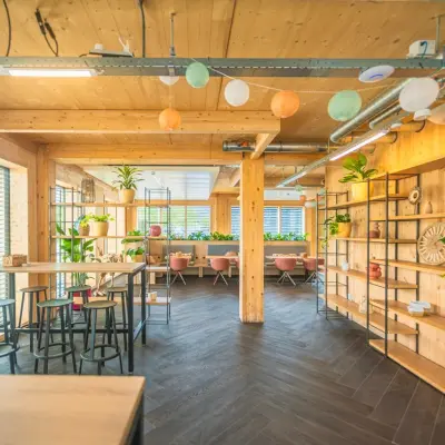 Bright, wooden-accented office space in Enschede featuring high tables and seating areas, ideal for office space rental. Abundant natural light and greenery enhance the ambiance.