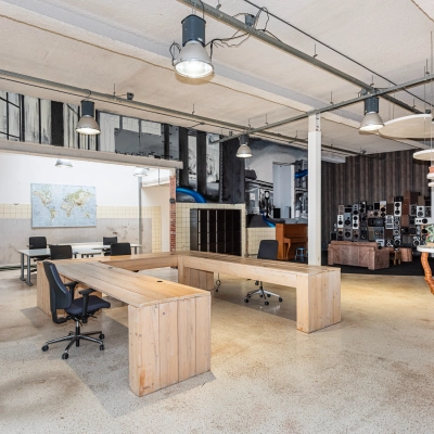 A spacious office with industrial decor and wooden desks arranged for workspace use. The office location is available for rent in Enschede.