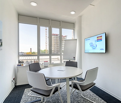 Bright office space with a round table and chairs, located at Mergenthaler Allee 15-21 in Eschborn, ideal for office space rental with large windows offering city views.