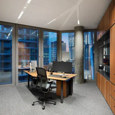 Modern office space with large windows, a wooden desk, ergonomic chair, and storage cabinets at Junghofstraße 9, Frankfurt Center; ideal for office space rental.