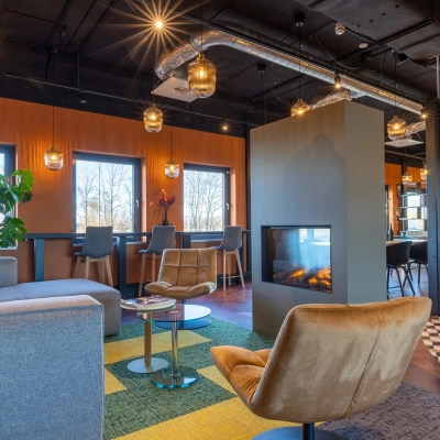 Furnished office space in Gouda at Zuidelijk Halfrond 1 with modern seating arrangements around a central fireplace, multiple tables, and ambient lighting. Ideal for office space rental.