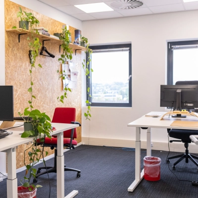 Bright, furnished office space in Gouda with desks and plants, ideal for office space rental. Neutral decor with large windows providing natural light and a view. Two red chairs add a pop of color.