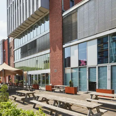Exterior view of the office at Helperpark 270-298, Groningen, featuring wooden picnic tables outside a modern building. Ideal for businesses seeking office space rental in a contemporary setting.