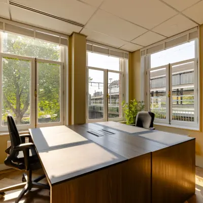Bright furnished office space for rent at Haarlem Centraal Station, featuring large windows and modern furniture, ideal for focused work.