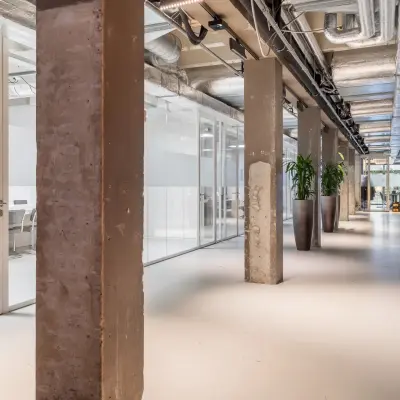 Industrial-style office space at A. Hofmanweg 5A, Haarlem Waarderpolder, featuring open corridors and glass dividers. Ideal for businesses seeking office space rental. Potted plants add a touch of greenery.