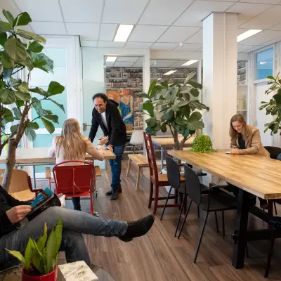 A furnished open-plan office space at Waarderweg 19, Haarlem Waarderpolder, features people working at tables surrounded by greenery. Ideal for those seeking office space rental.