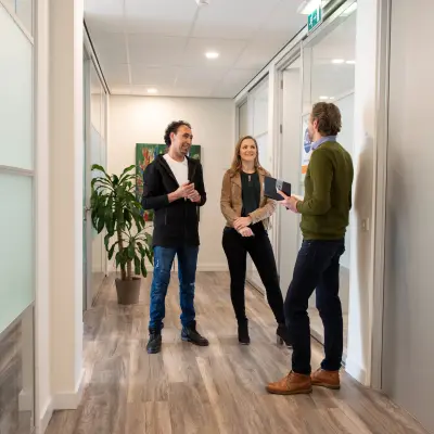 Three people engaged in a discussion in a modern office hallway at Waarderweg 19, highlighting the collaborative environment of this office space rental in Haarlem Waarderpolder.