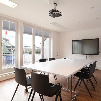 Bright office space with large windows, a table, chairs, and a TV, perfect for meetings. Ideal office space rental at Colonnaden 5, Hamburg Neustadt.