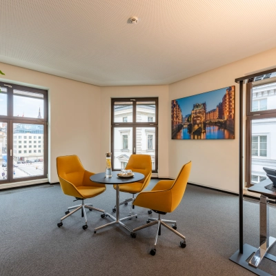 Well-lit office to rent at Alter Wall 32, Hamburg Old Town, featuring a small meeting area with chairs and desk, ideal for business discussions.