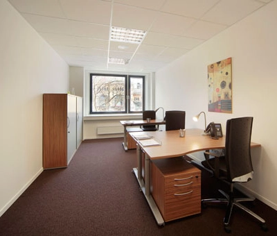 A bright office space with two desks, chairs, and a cabinet, located at Bahnhofstraße 8 in Hannover Mitte. Ideal for office space rental with natural light from large windows.