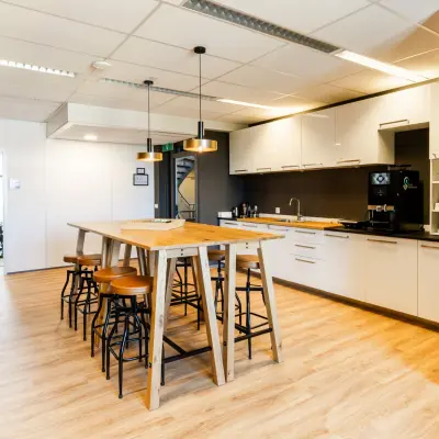 Modern office kitchen area with wooden table, bar stools, and equipped kitchen facilities at Demmersweg 3 in Hengelo, ideal for office space rental.