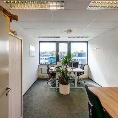 Interior view of an office space available for rent at Welbergweg 60, Hengelo, featuring desks, chairs, and natural light through large windows.