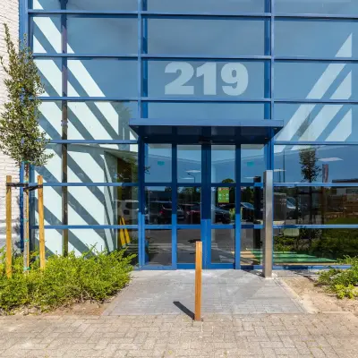 Entrance of an office building at Franciscusweg 219, Hilversum, showcasing modern glass architecture with visible office space rental opportunities.