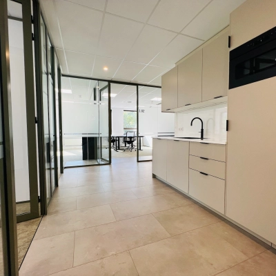 Modern office space available for rent in Hilversum's Marathon 2, featuring a sleek kitchenette beside spacious workspaces.