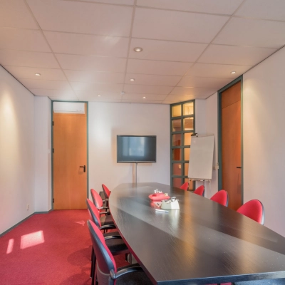 Office space for rent at Mozartlaan 27, Hilversum, featuring a conference room with a long table, red chairs, a TV, and a whiteboard.