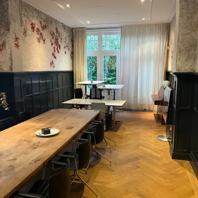 Interior view of a furnished office space for rent at Oude Enghweg 8, Hilversum, featuring wooden tables and black chairs under soft lighting.