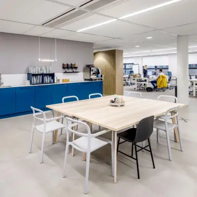 Furnished office space in Hoofddorp with blue cabinetry and a communal table, surrounded by people working at desks. Ideal for office space rental.