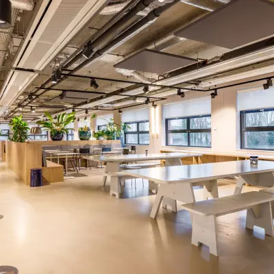 Spacious and modern office interior at Siriusdreef 16, Hoofddorp, featuring furnished workspaces with tables, benches, and greenery. Ideal office space rental opportunity.