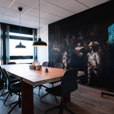 Cozy office space for rent in Hoogeveen featuring a large wooden table and modern chairs, ideal for meetings. A bright mural and a TV add a stylish touch to the room.