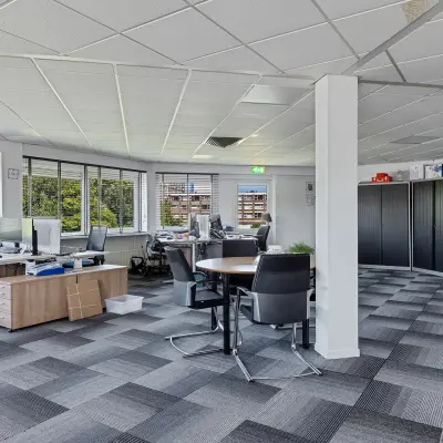 Modern office space in Leeuwarden at Ouddeelstraat 7a with desks and chairs, ideal for rent. The office to rent features large windows providing natural light and a neutral carpet design.