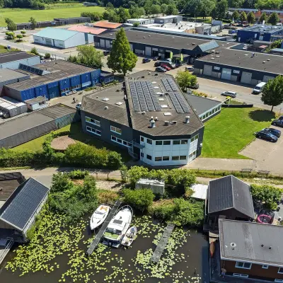 Overhead view of an office building at Ouddeelstraat 7a, Leeuwarden, surrounded by greenery and industrial buildings. Ideal for office space rental with ample parking opportunities.