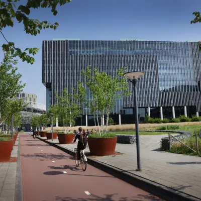 Exterior view of offices for rent at Bargelaan 200, Leiden, showcasing modern architecture with plant-lined walkways. People are walking and cycling outside.