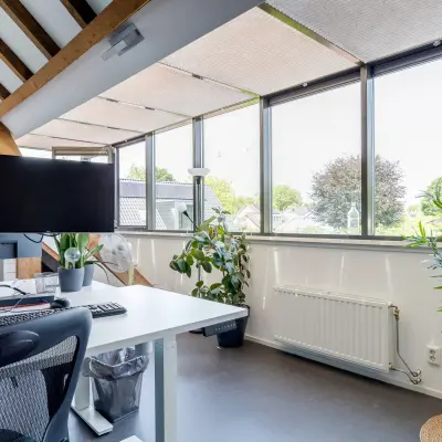 Bright, furnished office space with large windows, plants, and workstations available for rent at Hamersveldseweg 120, Leusden.