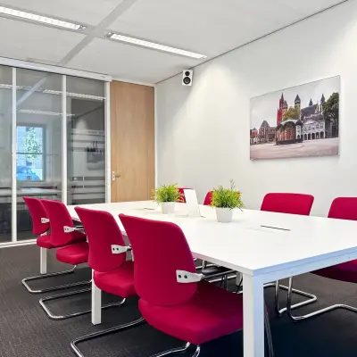 Bright office space at Robert Schumandomein 2, Maastricht, featuring a meeting table with vibrant red chairs and potted plants, ideal for office space rental.
