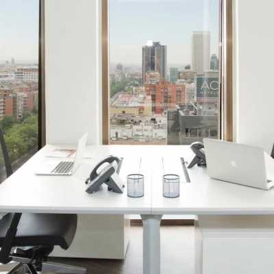 Bright office space with two desks, chairs, and a view of Madrid's skyline from Paseo de la Castellana 141. Perfect for rent office space seekers.