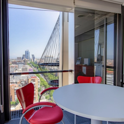 Office space for rent at Paseo de la Castellana 95, Madrid Azca, featuring a round white table and red chairs with a panoramic city view.