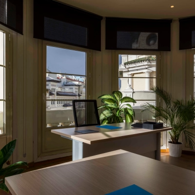 Bright office space rental at Calle Gran Vía 6, Madrid Center, featuring modern desks, lush plants, and large windows offering scenic city views. Ideal office to rent for professionals seeking an inspiring environment.