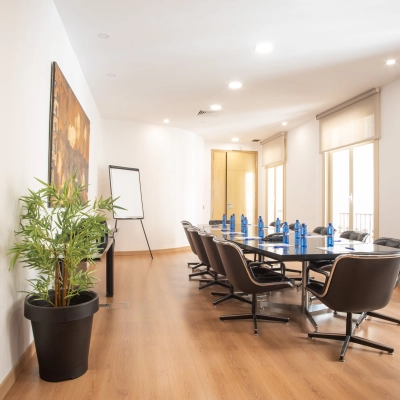 Bright office space rental at Calle Gran Vía 6, Madrid Center featuring a furnished meeting room with a long table, chairs, and a flip chart.
