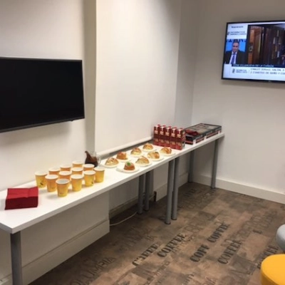Cozy office lounge with a long table set for snacks, beverages, and a wall-mounted TV. Ideal for office space rental in Calle Capitan Haya 60, Madrid Tetuán.