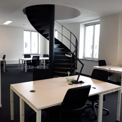 Modern office space with spiral staircase at Kardinaal Mercierplein 2 in Mechelen Centrum, available for rent. Features multiple desks and chairs, creating an inviting workspace atmosphere.